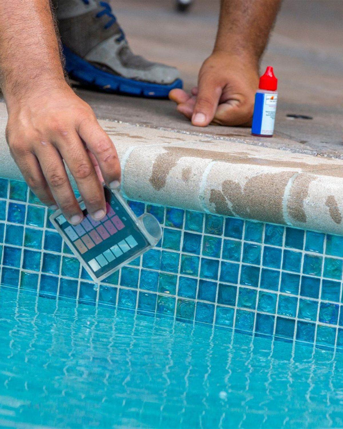 Miracle Pool Care technician testing pool water beside blue waterline tile