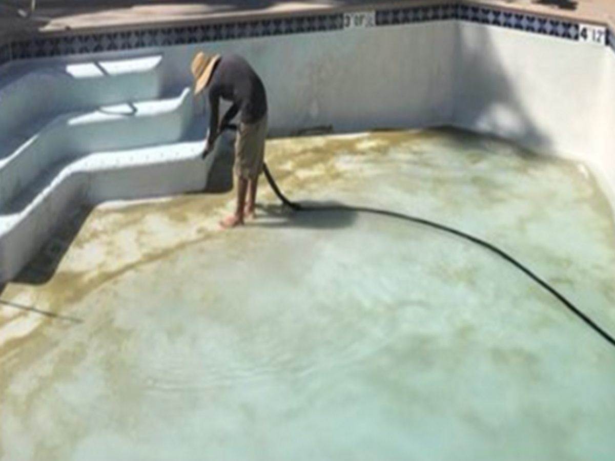 Drained pool floor covered in green and brown staining before an acid wash