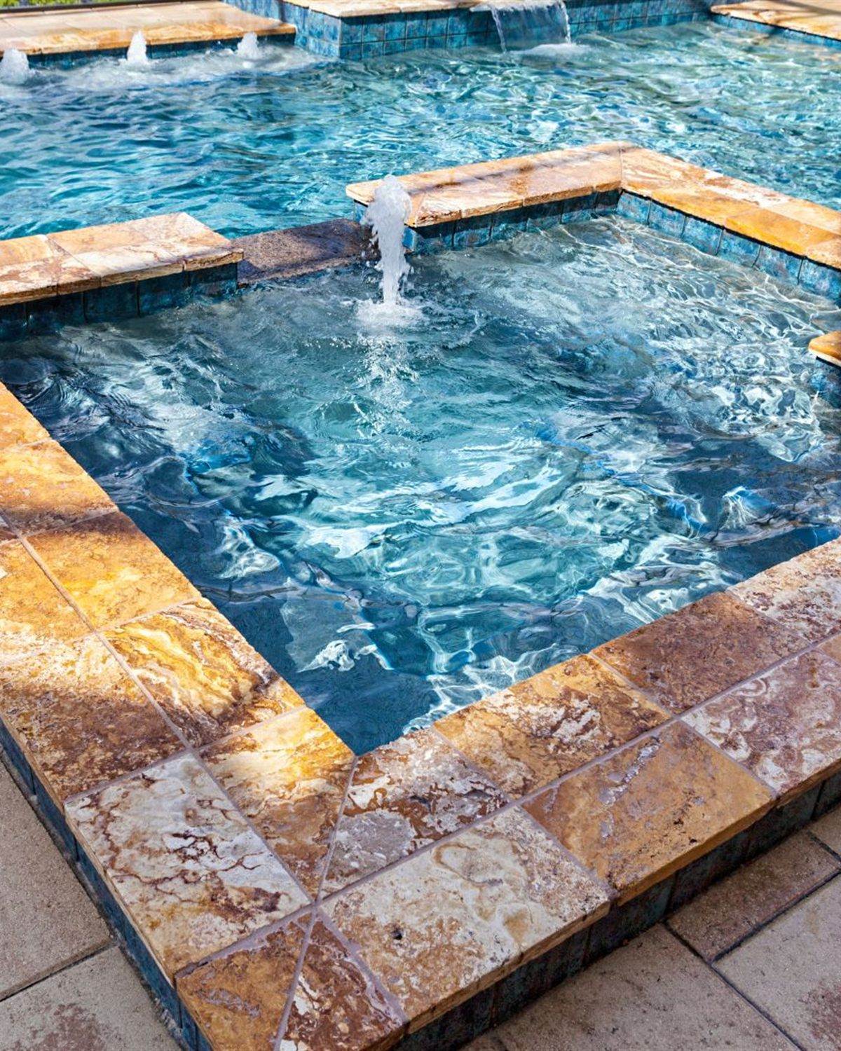 Raised spa with blue waterline tile spilling into a clear backyard pool in Buckeye, AZ