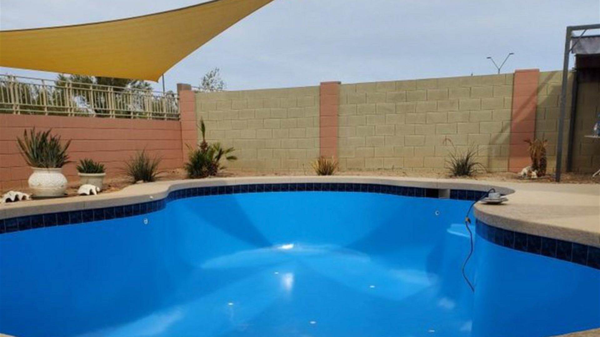 Freshly epoxy-coated blue pool in an Arizona backyard with shade sails