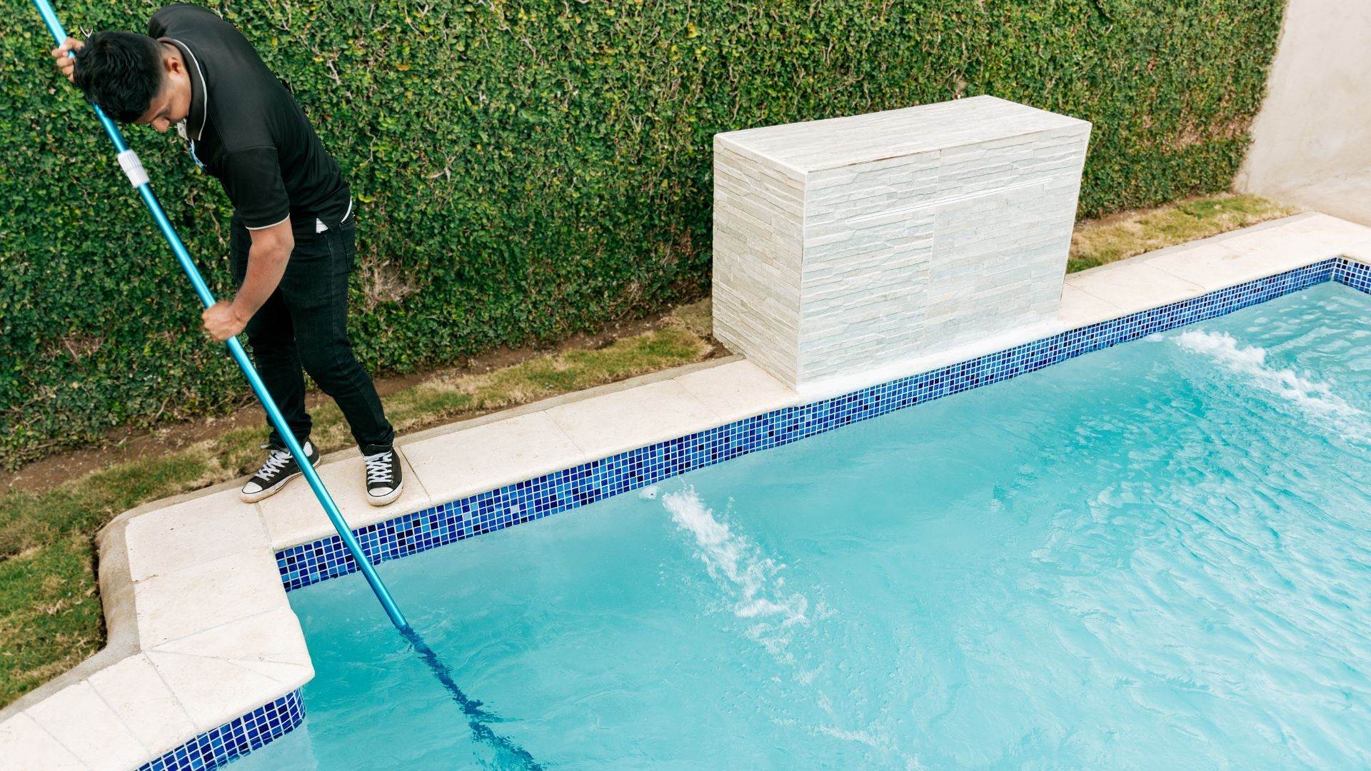 Pool technician vacuuming a rectangular pool on a weekly service visit