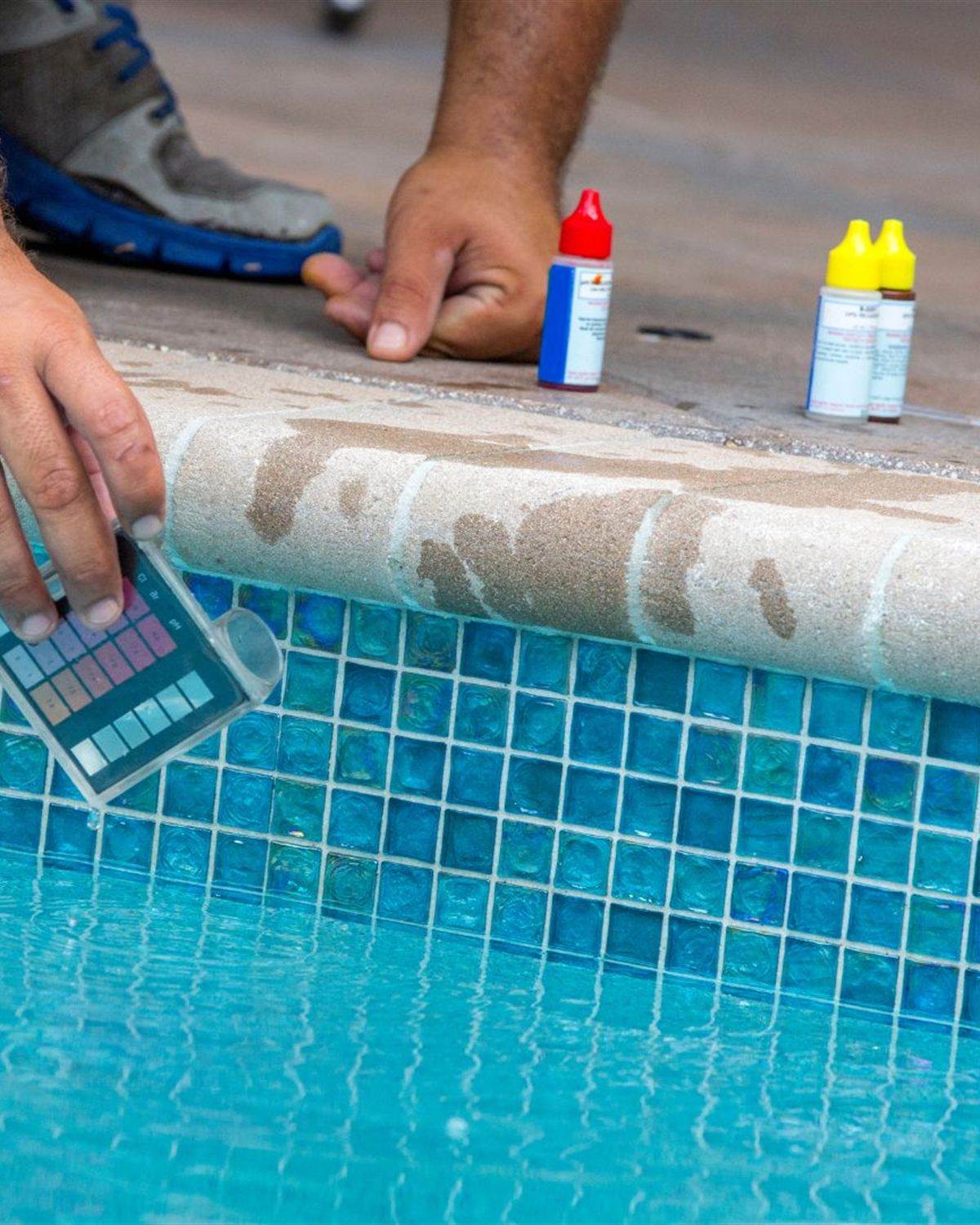 Pool technician testing water chemistry beside a residential pool