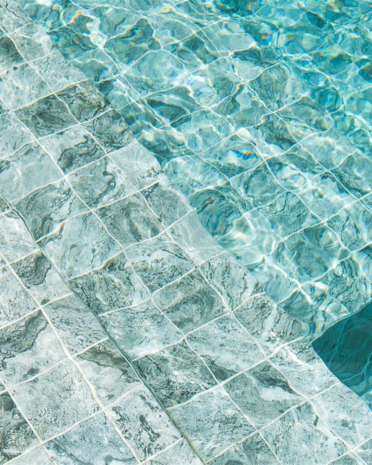 Pale marble-look pool steps seen underwater with clean, unstained surfaces