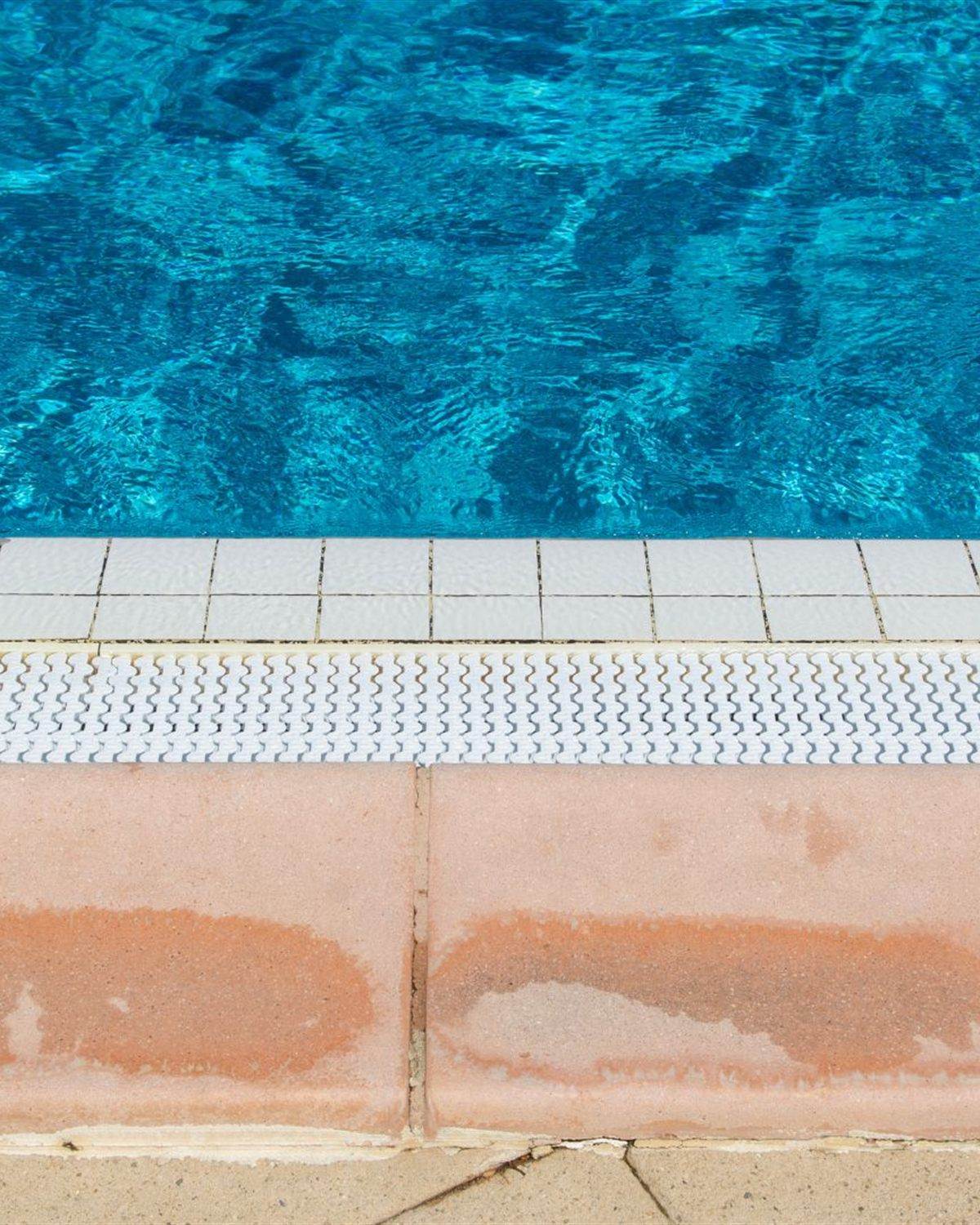 Pool coping and terracotta pavers showing dark water staining before washing