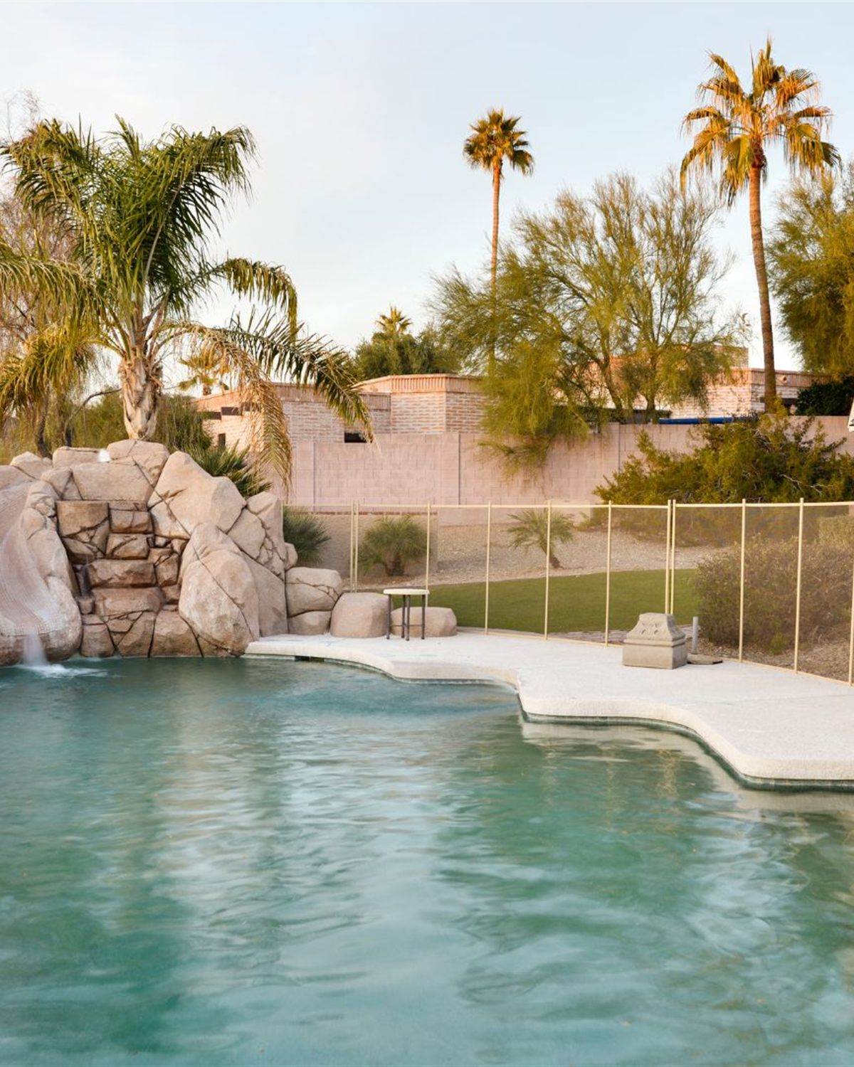 Backyard pool with a rock waterfall and safety fencing