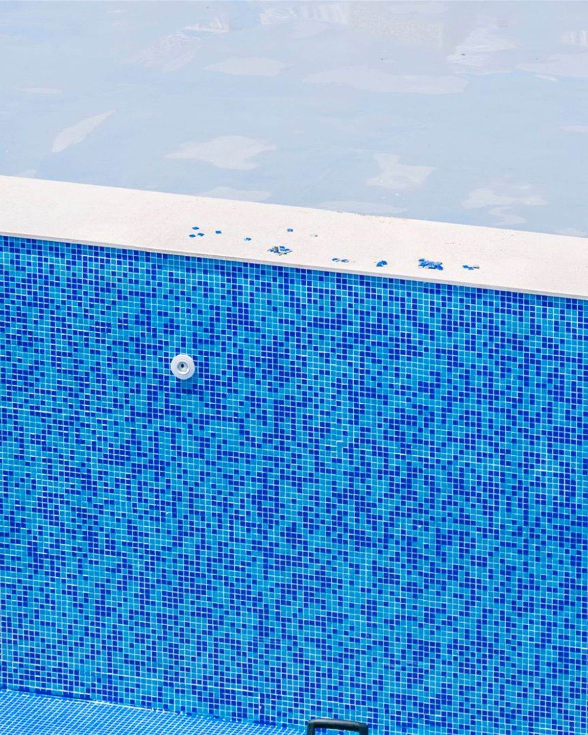 Empty pool with mosaic tile walls and a deck brush leaning against the side