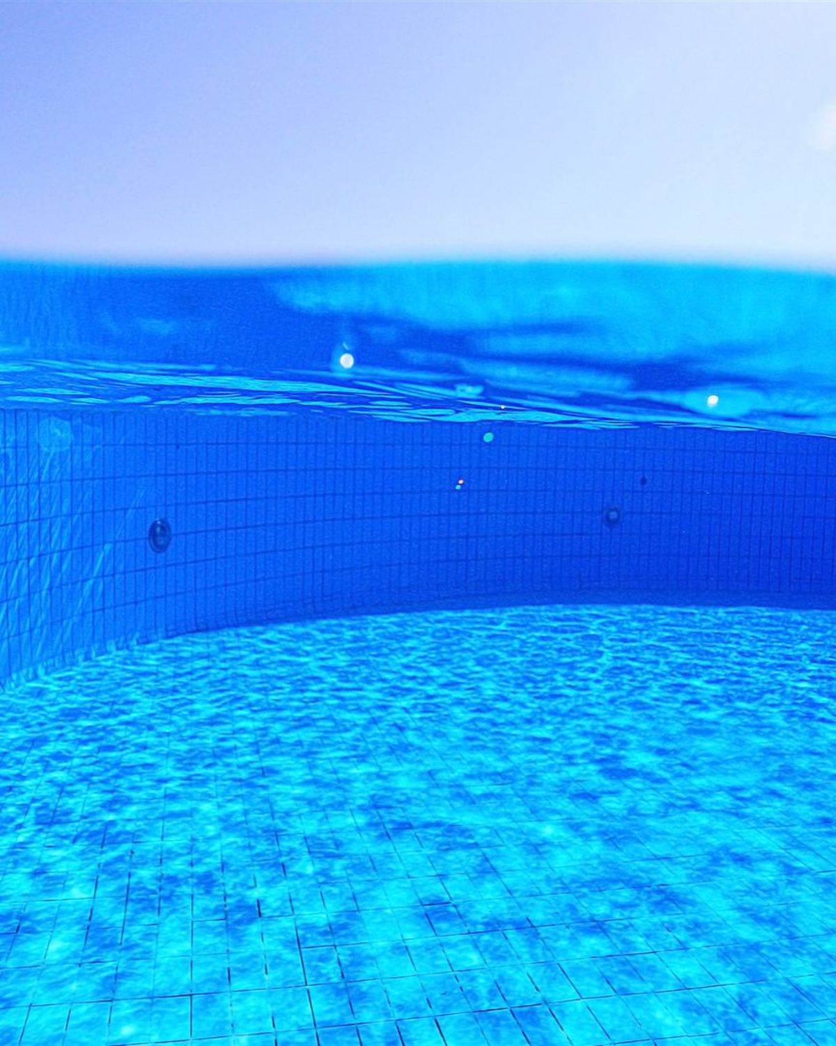 Underwater view of a blue tiled pool interior looking toward the surface