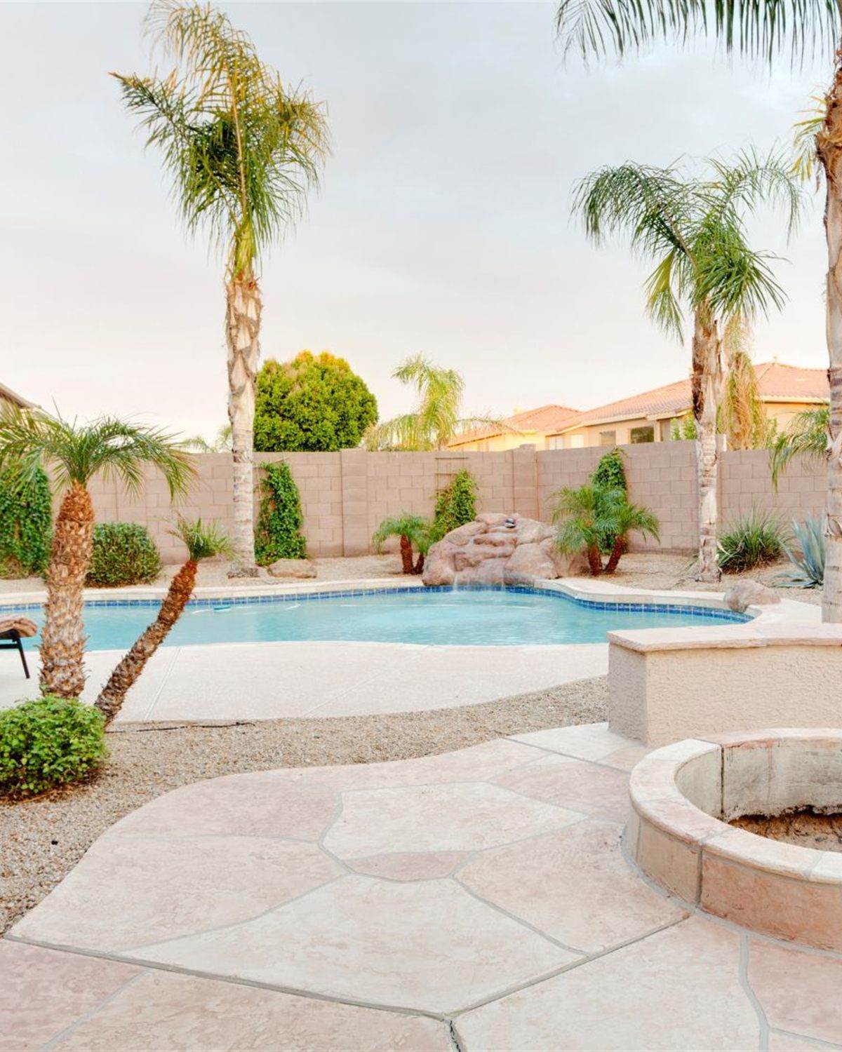 Wide flagstone patio with a stucco fire pit and queen palms in a Phoenix-area backyard