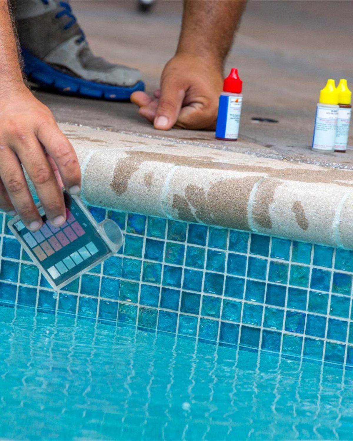 Technician testing pool water with a comparator block beside blue waterline tile