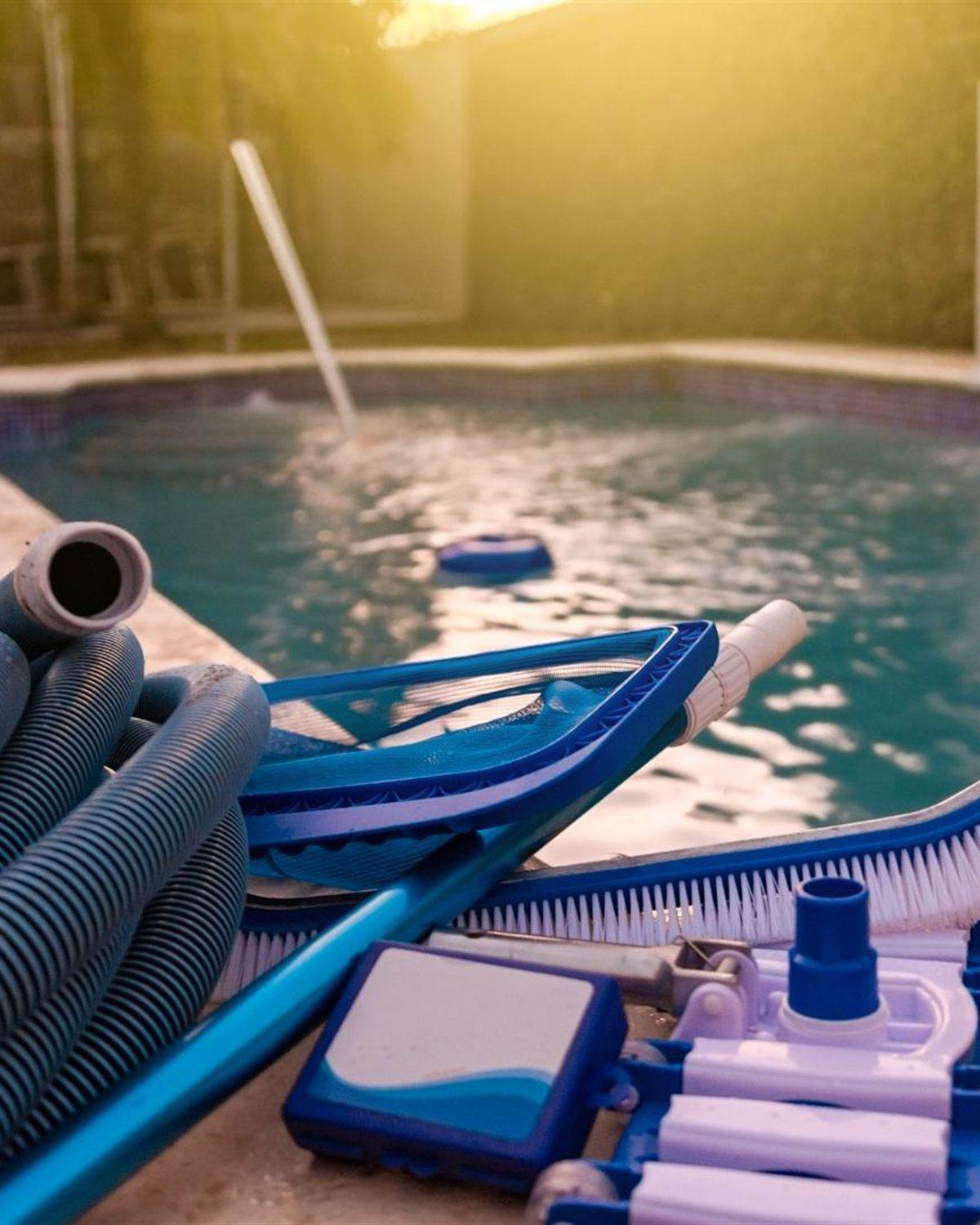 Pool net, brush and vacuum head arranged on pool coping at sunset